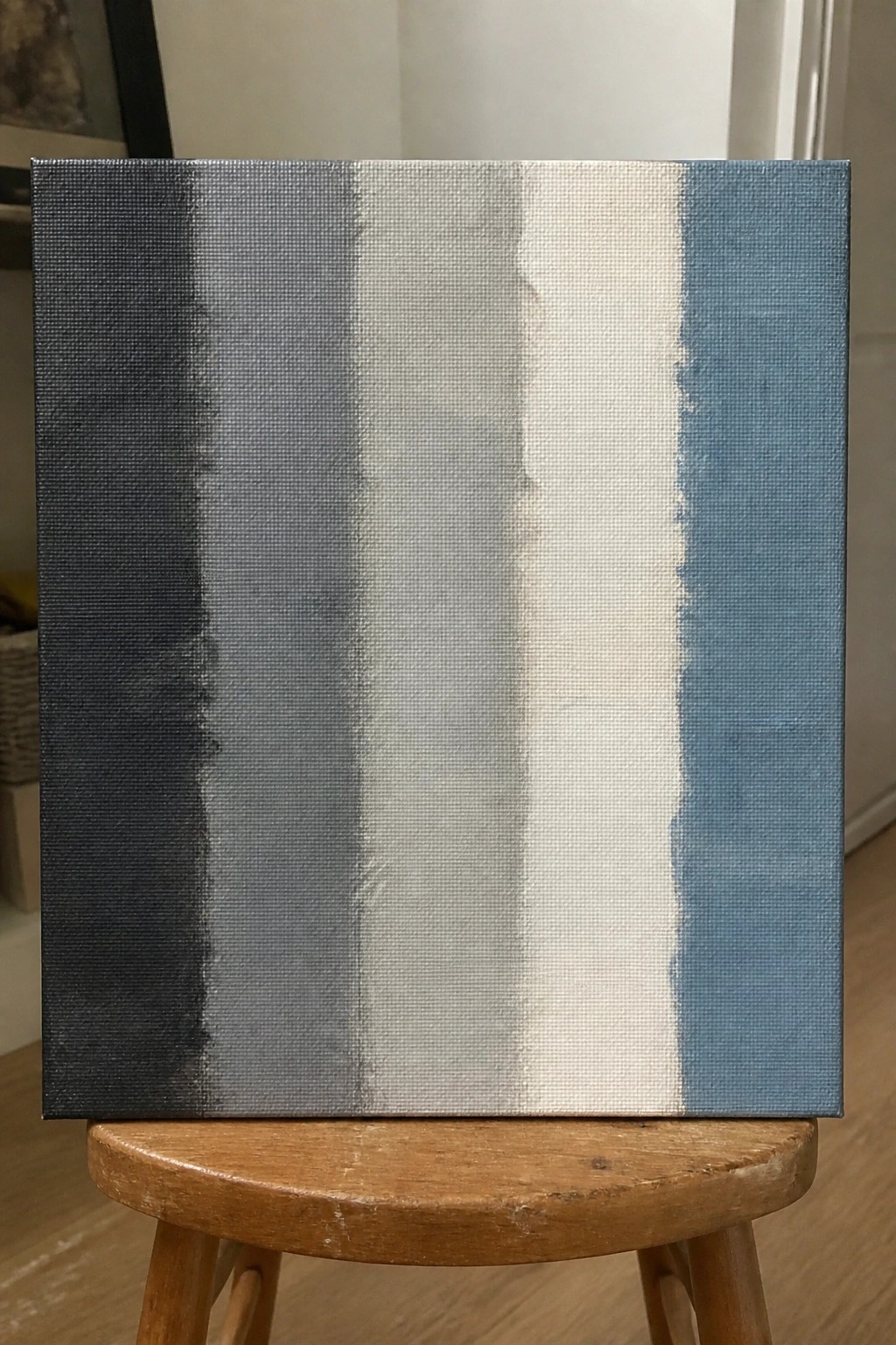 Abstract canvas with vertical black gray white and blue stripes on wooden stool