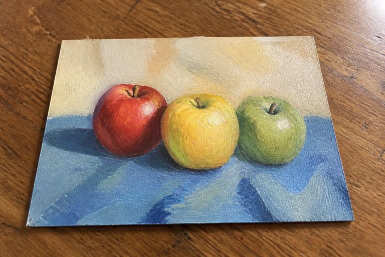 Still life oil painting of yellow, red, and green apples on blue cloth.