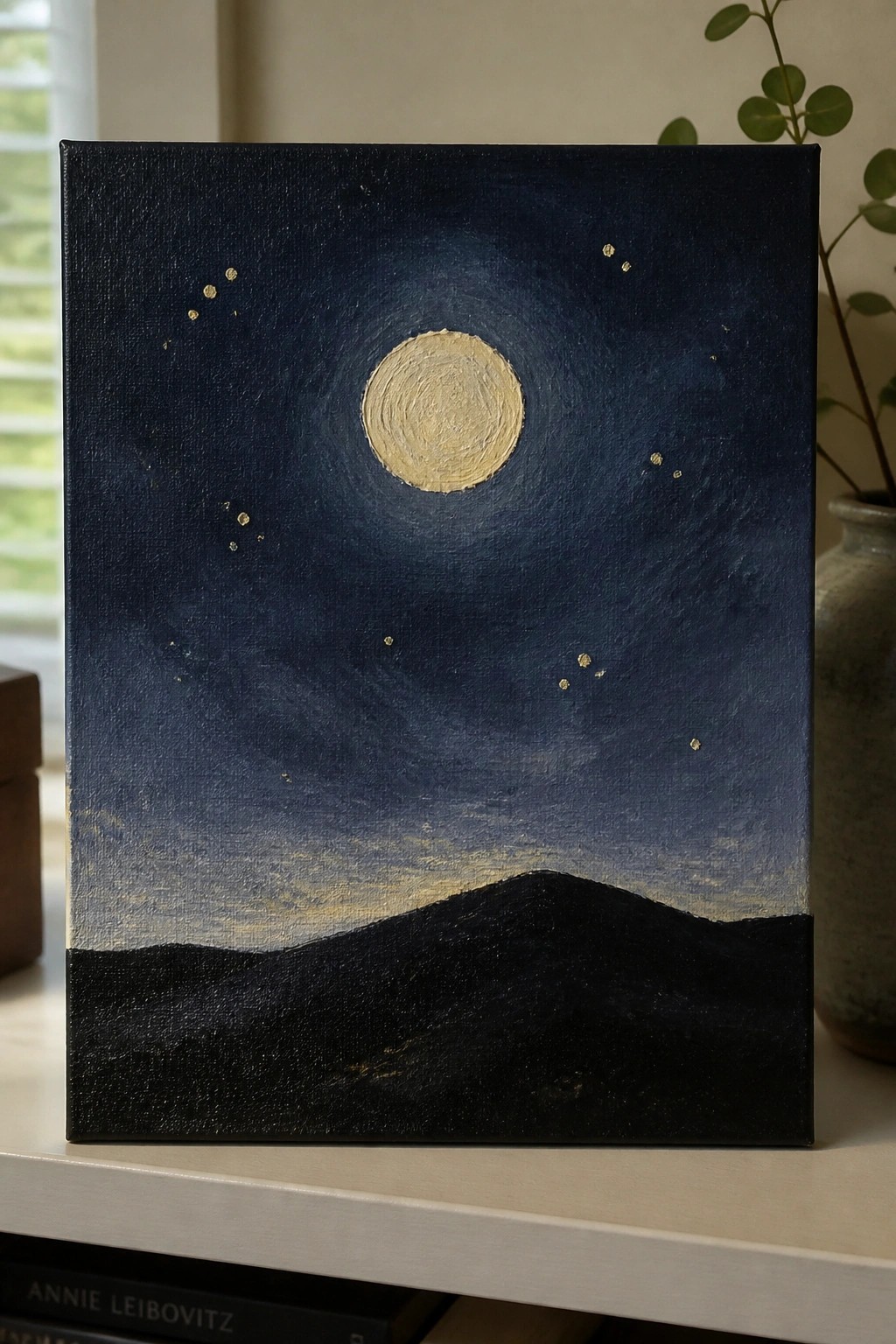 Night sky painting with glowing moon, gold stars, and black mountains on canvas
