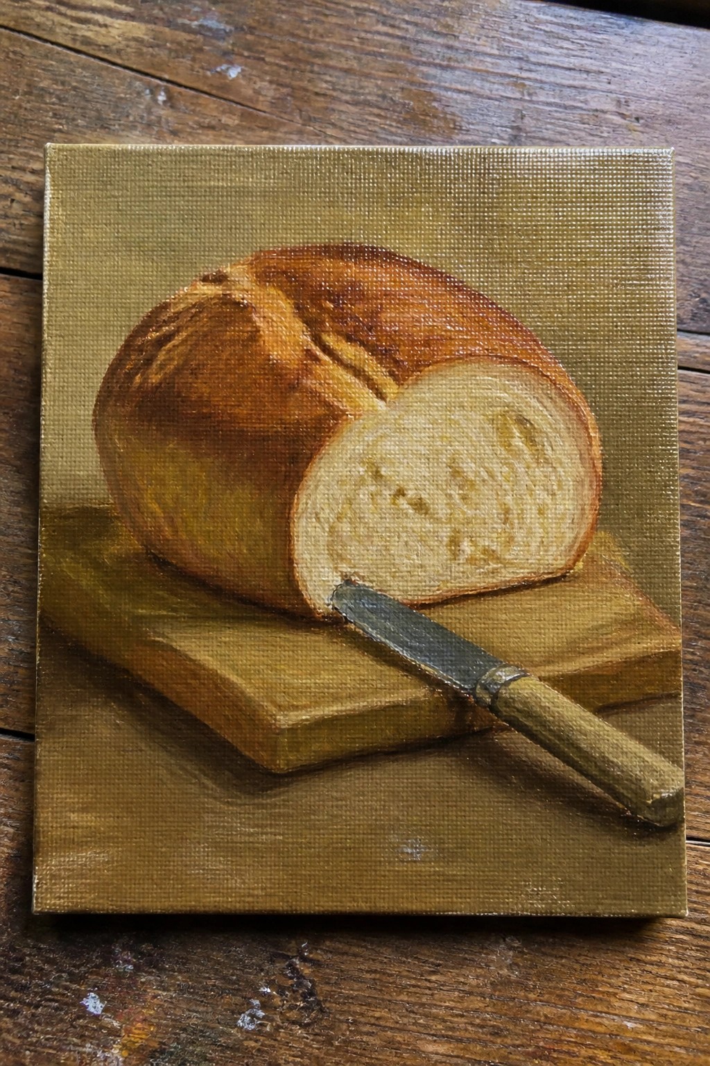 Oil painting of golden brown bread loaf sliced with knife on wooden boards.