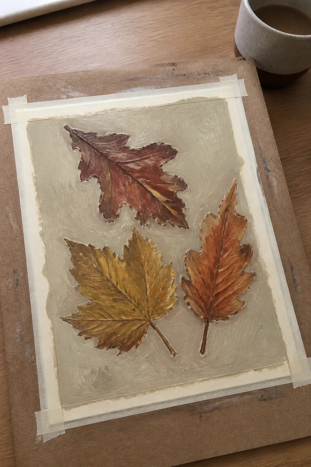 Three autumn leaves in red, yellow, and orange painted on taped paper over wood.
