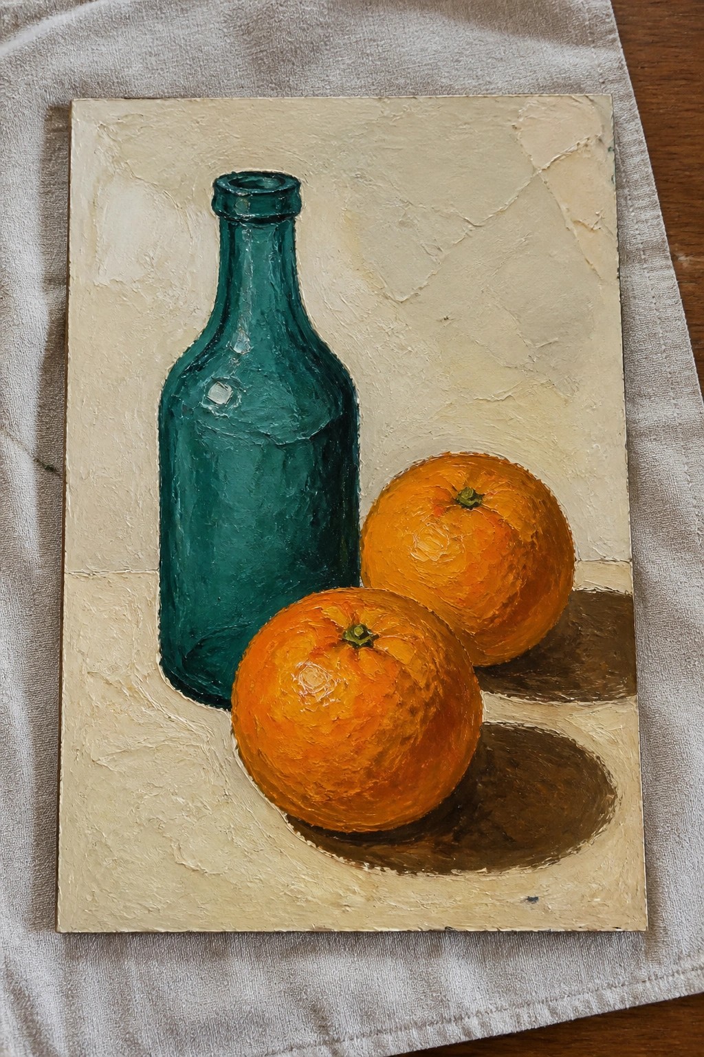 Still life painting of a teal bottle and two oranges with shadows.