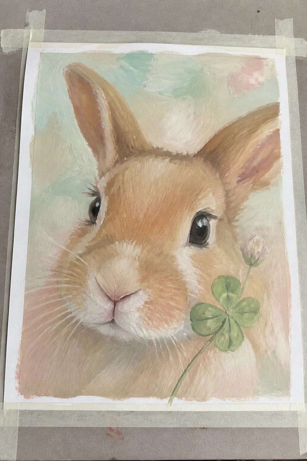 Close-up painting of a brown rabbit holding a four-leaf clover in soft pastels.