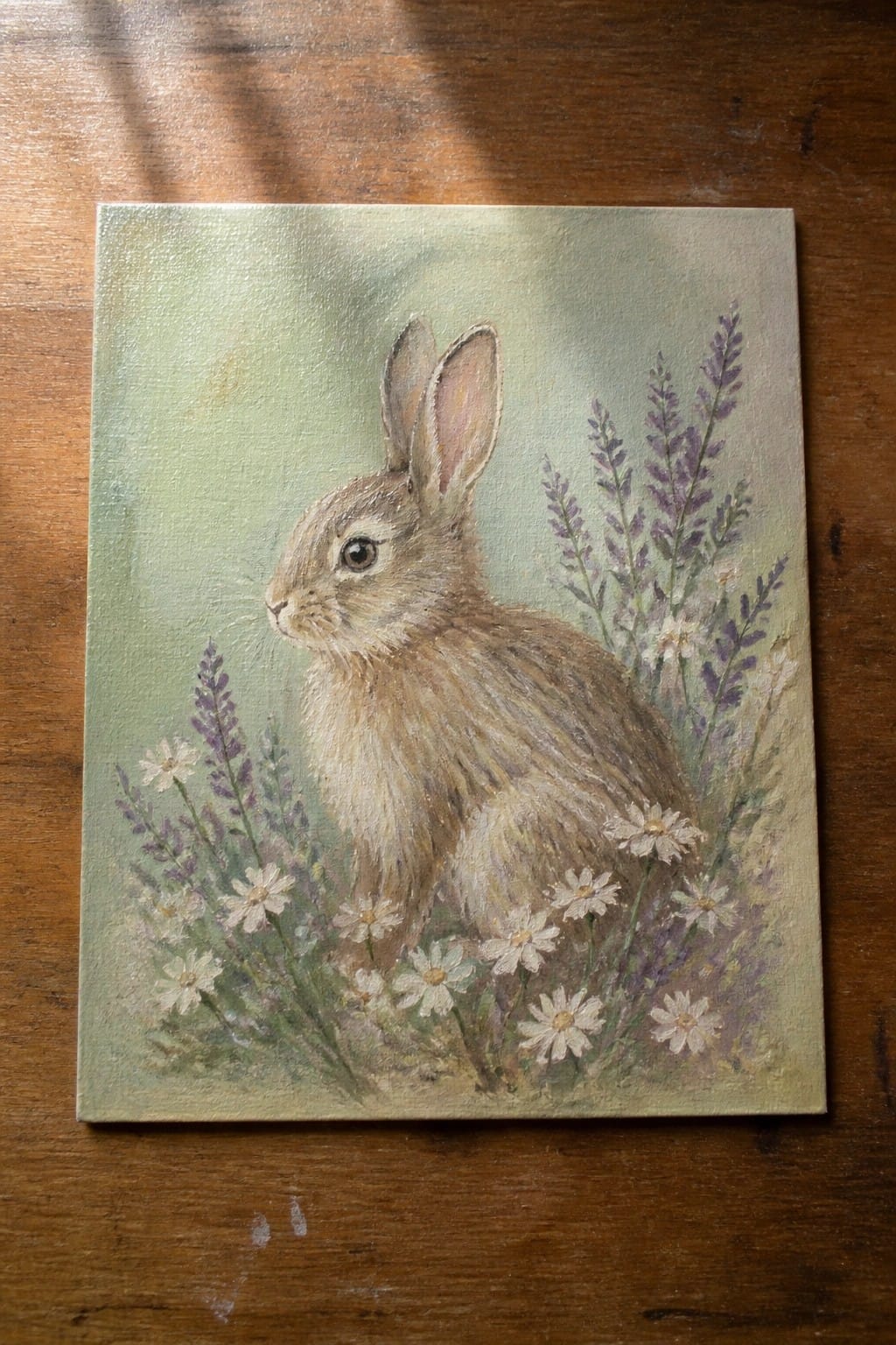 Brown rabbit nestled among white daisies and purple lavender in soft green painting.