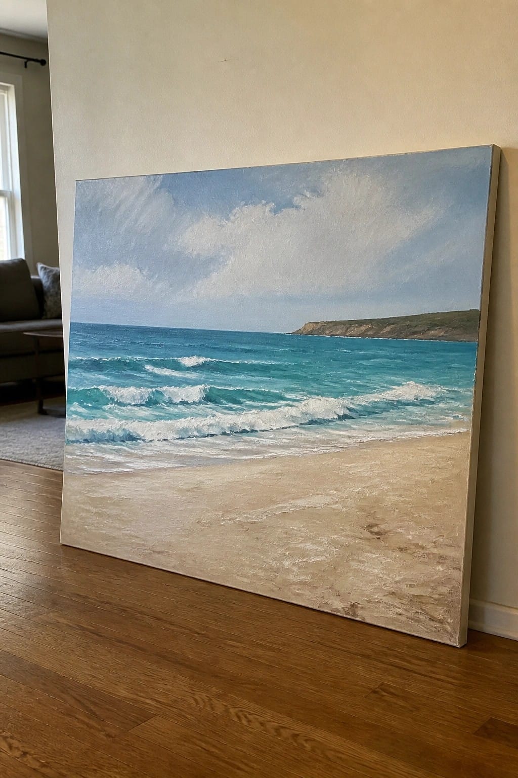 Large seascape painting of turquoise waves on sandy beach leaning against wall indoors