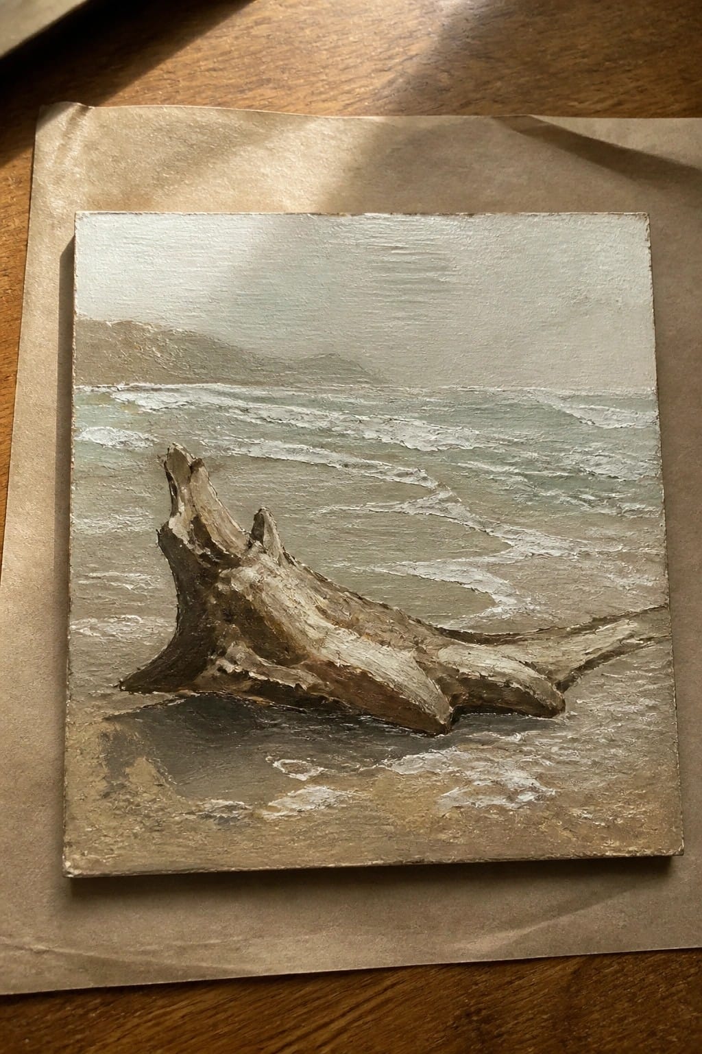 Weathered driftwood rests on a sandy beach amid gentle ocean waves and misty hills.