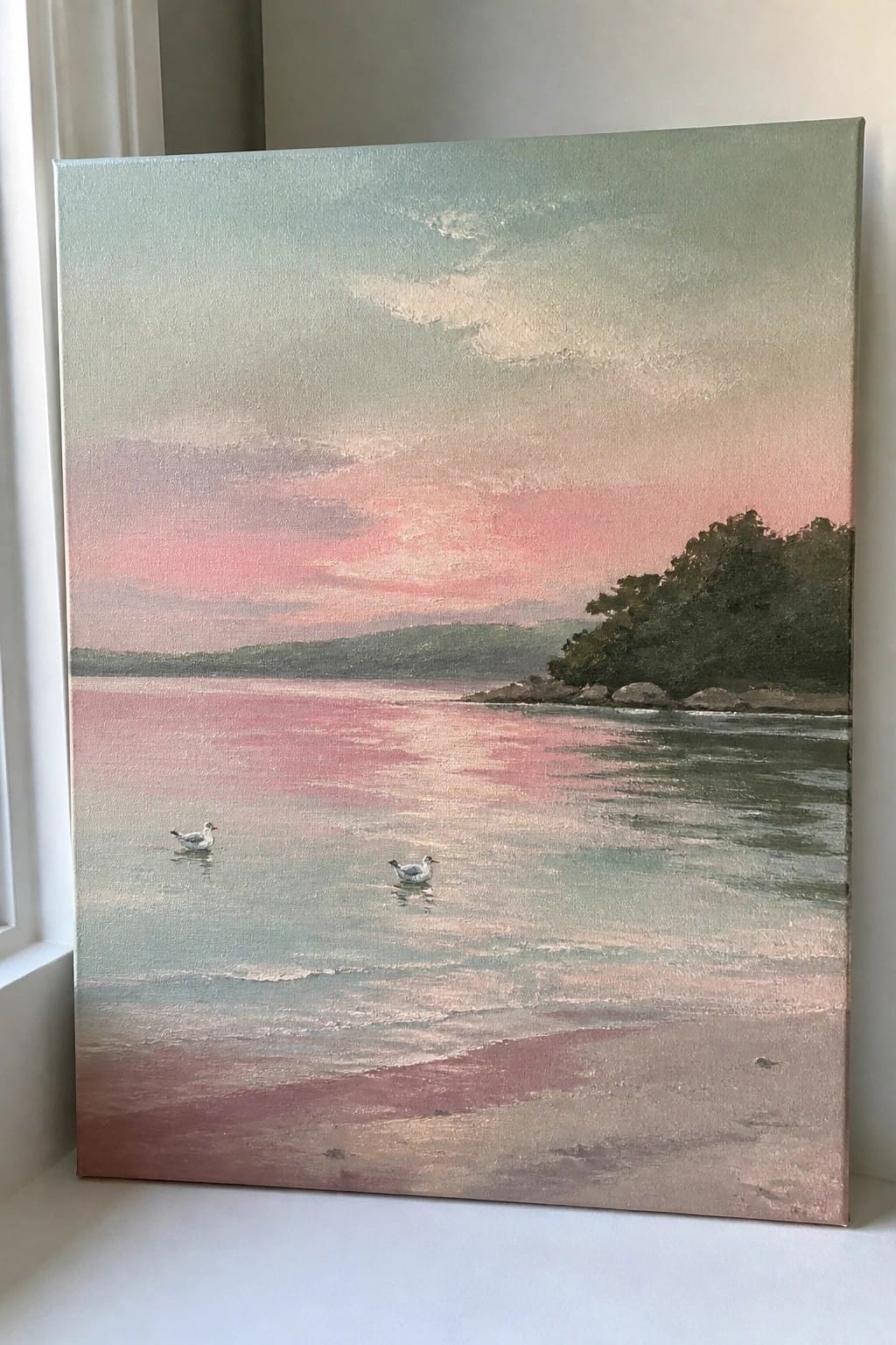 An oil painting of a pink and green sunset over calm water with two seagulls, a sandy foreground, and distant tree-covered land.