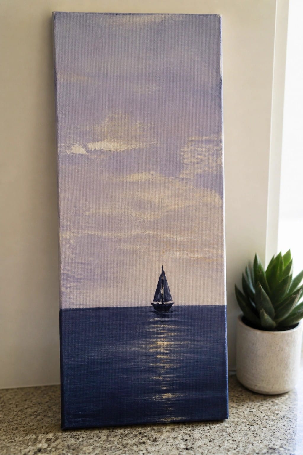 Canvas painting of sailboat on calm waters under purple sky beside succulent plant.