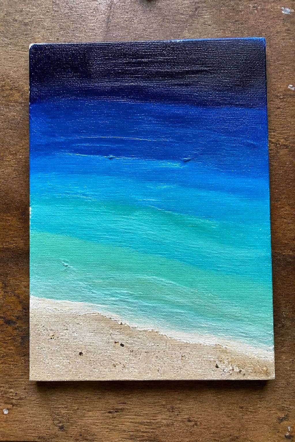 Painting of blue ocean waves fading to turquoise near sandy beach.