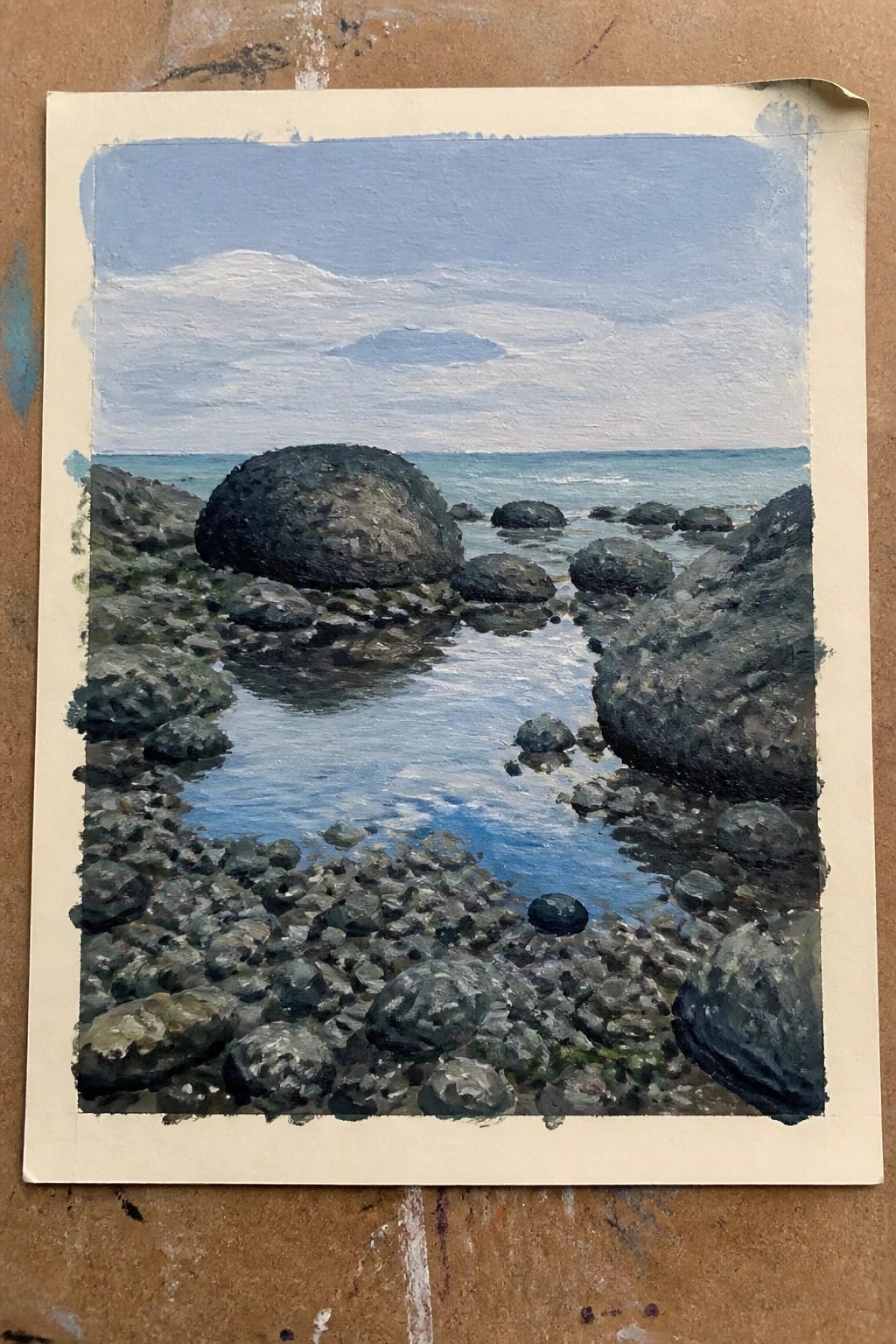 Oil painting of rocky shoreline with blue stream flowing into the sea.
