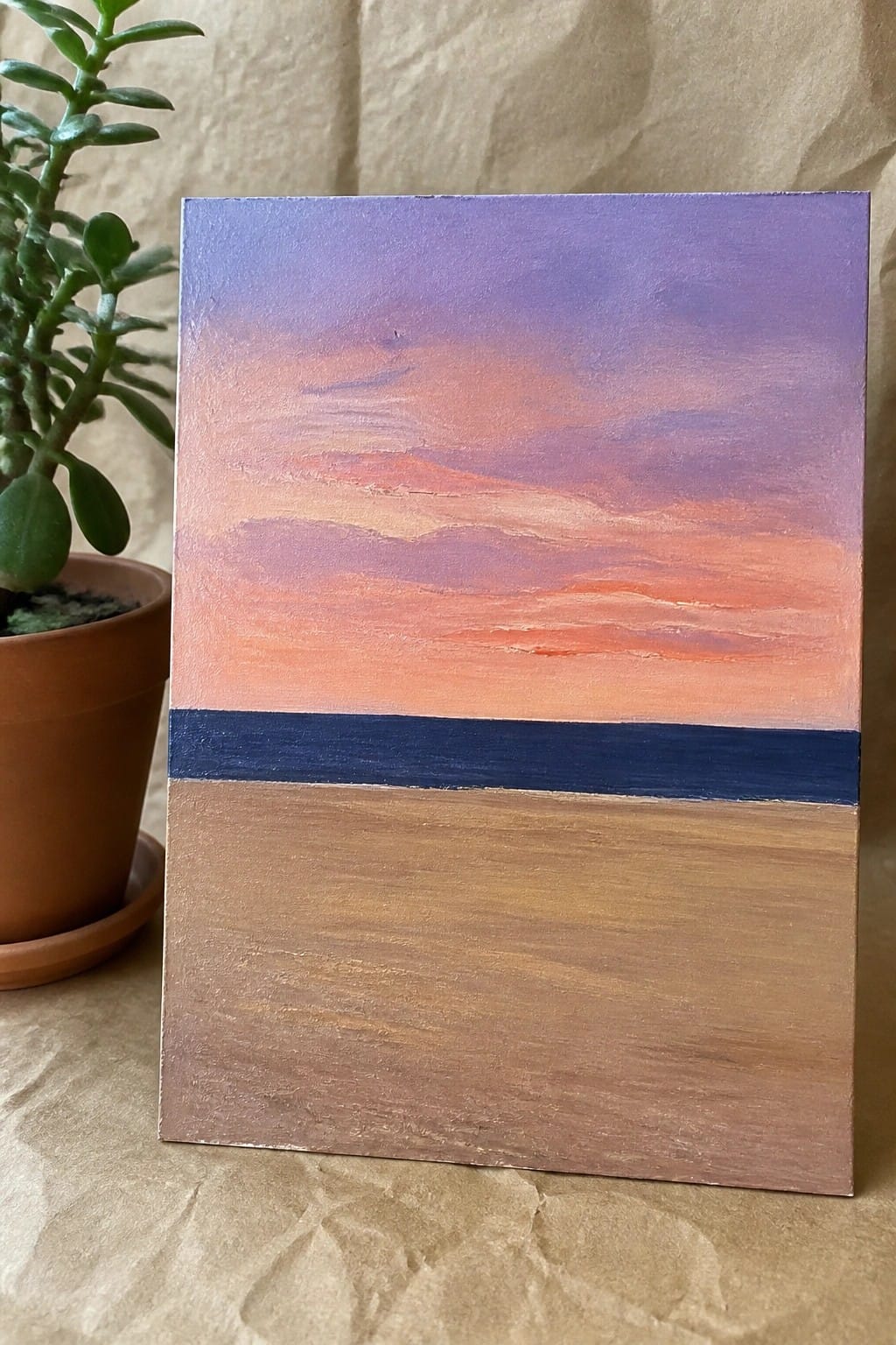 Painting of purple-orange sunset sky above blue horizon and brown foreground beside potted plant