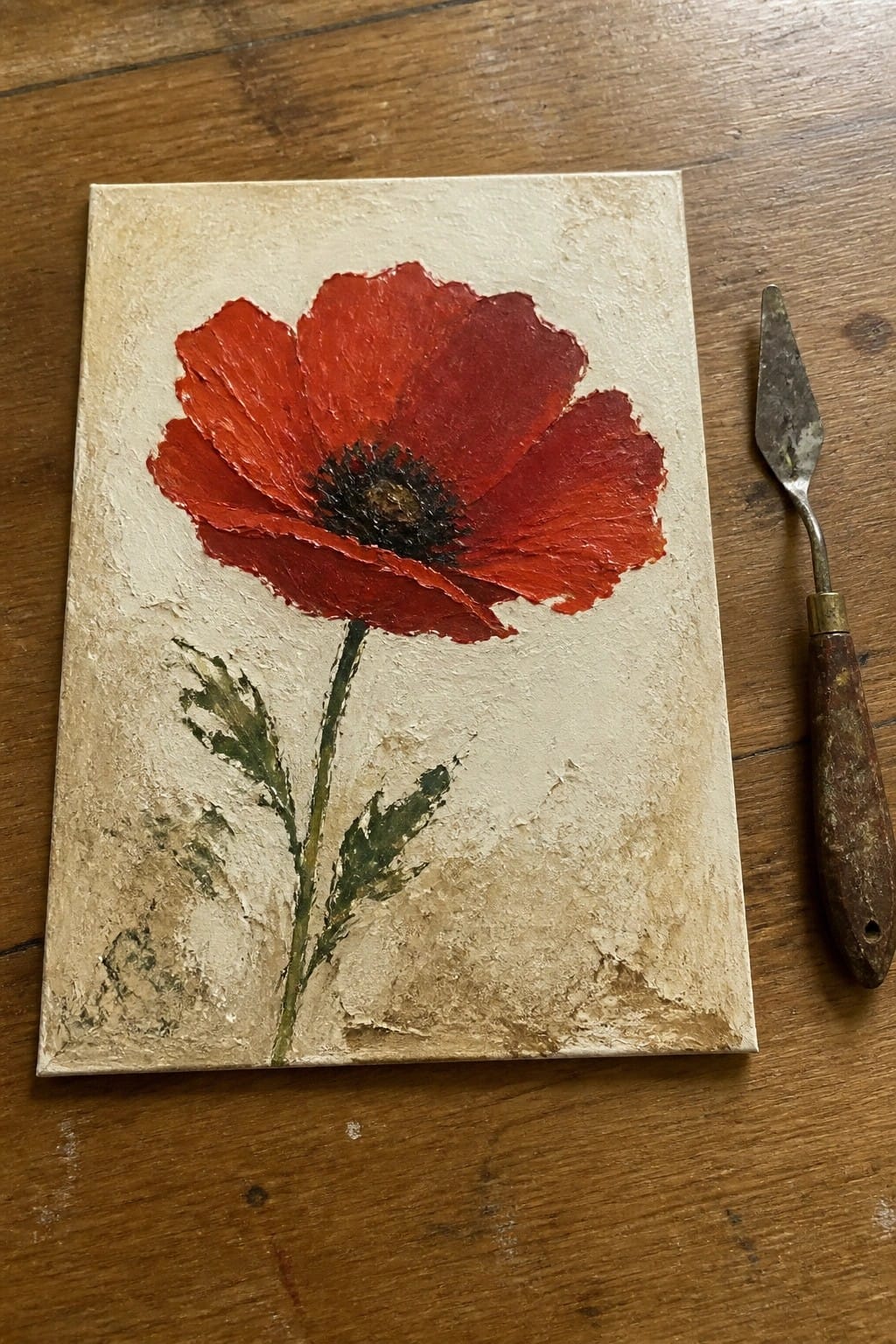Impasto red poppy painting on canvas beside palette knife on wooden table