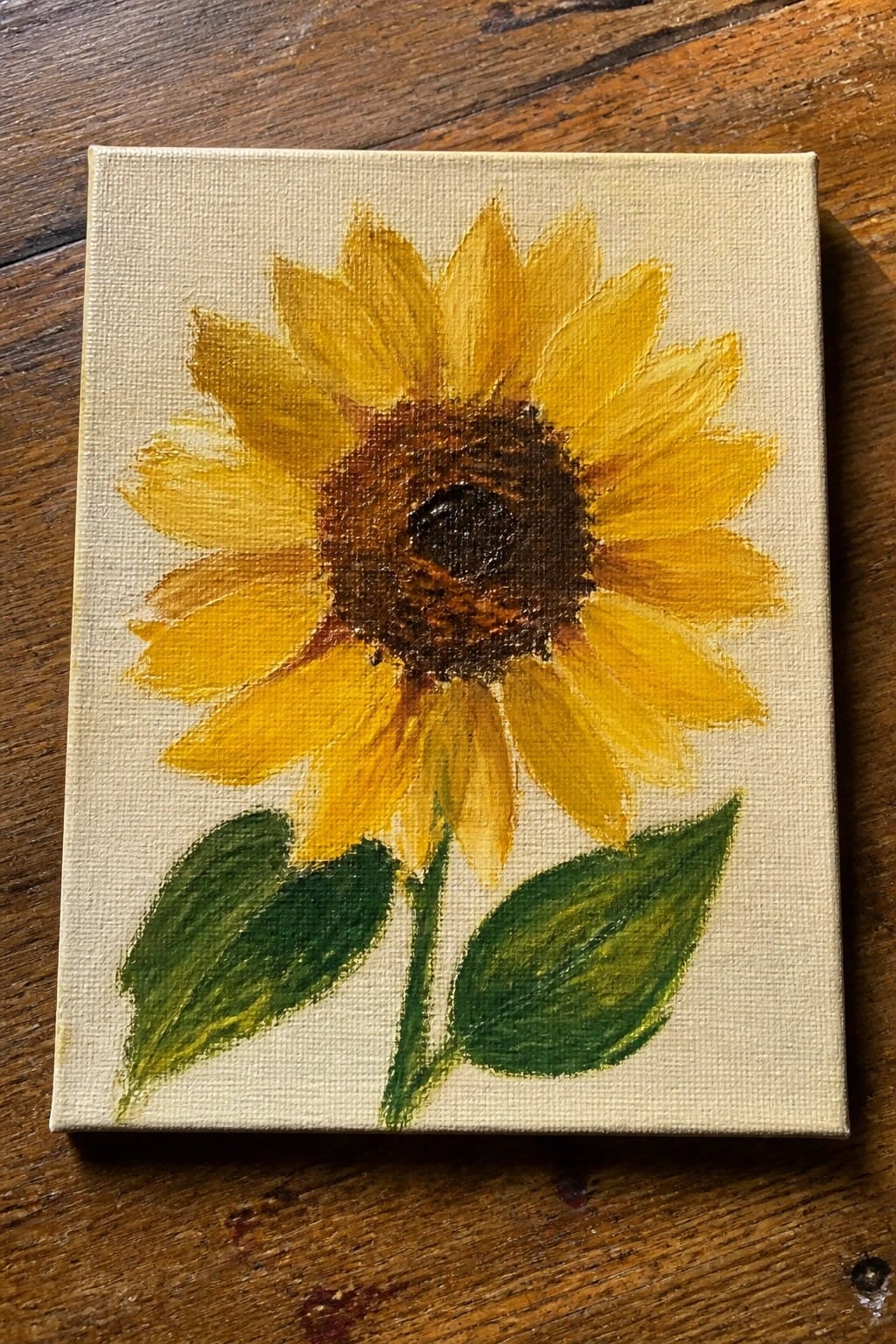Sunflower painting with yellow petals, brown center, green leaves on canvas.