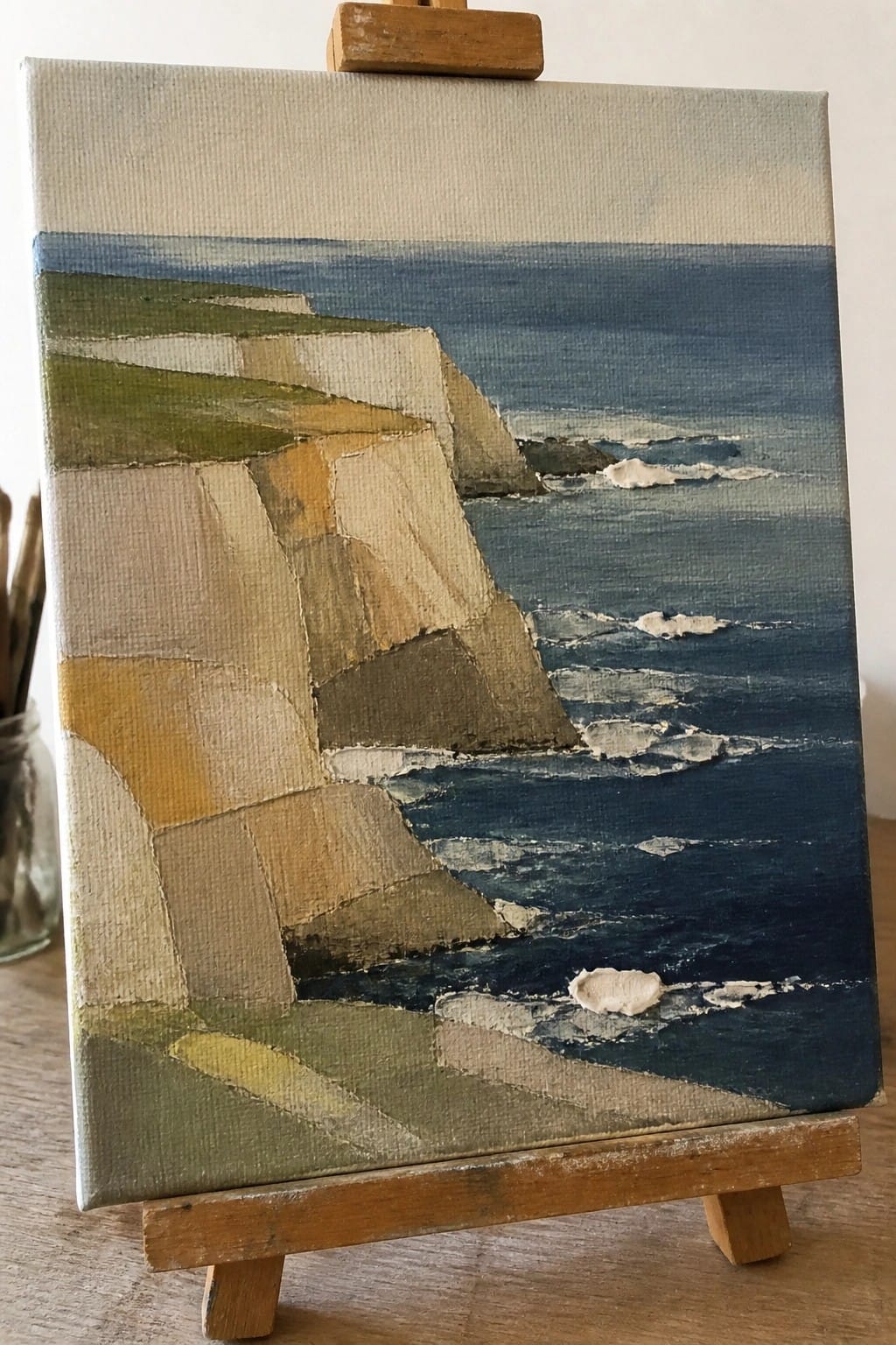 Abstract painting of cliffs and blue ocean waves on wooden easel.