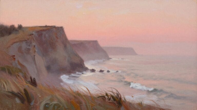 Pink-hued cliffs overlooking misty ocean waves with dry grass in foreground