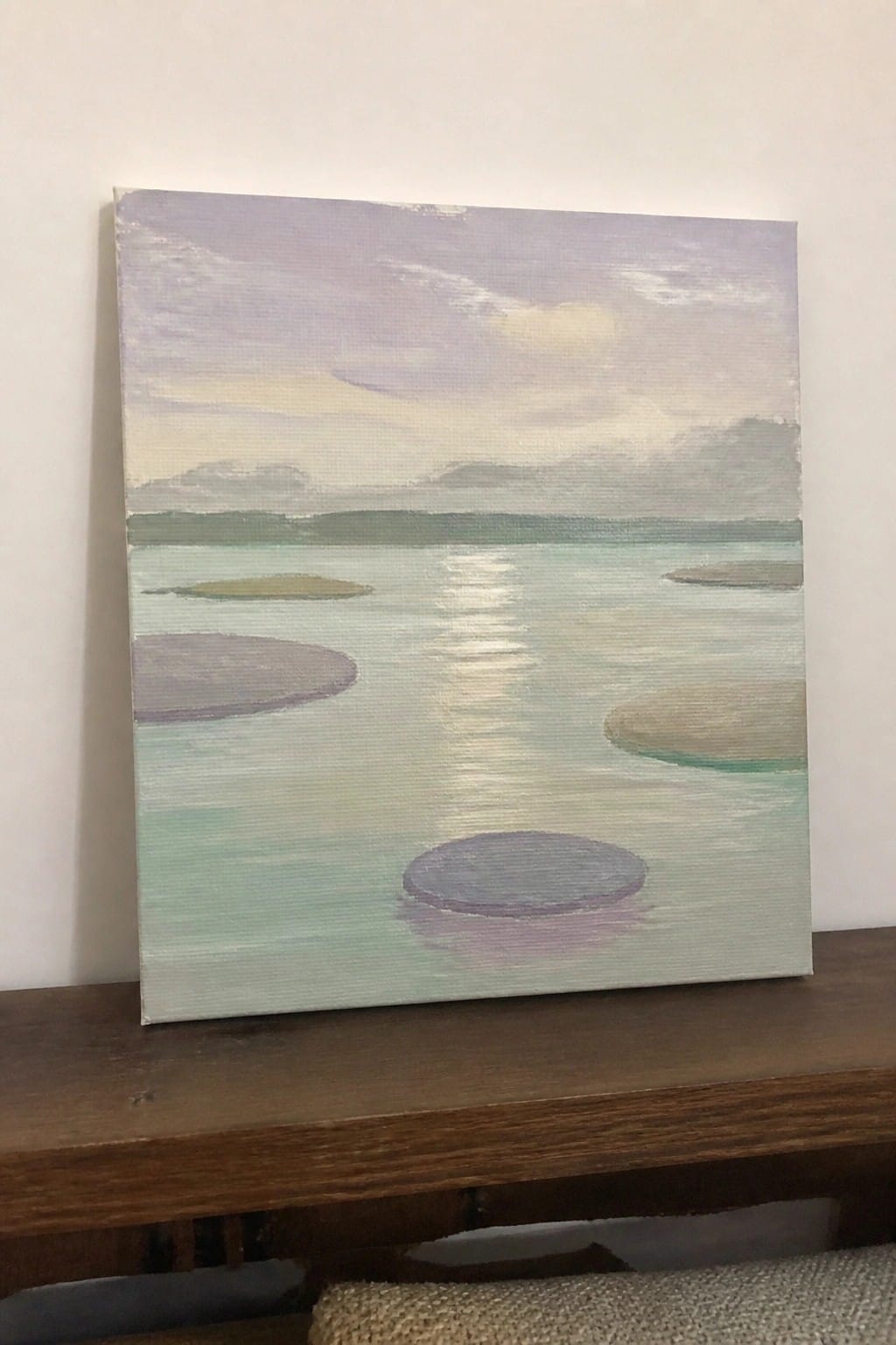 Painting of a lake with colorful circular islands under a purple sky on wood.