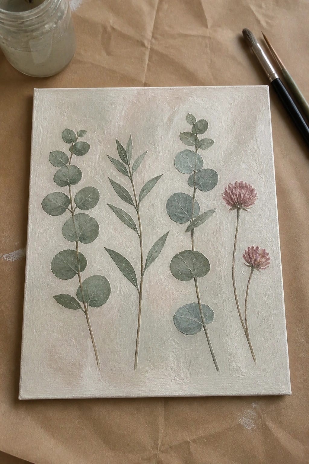 Botanical canvas painting of green eucalyptus leaves and pink clover flowers with paint supplies