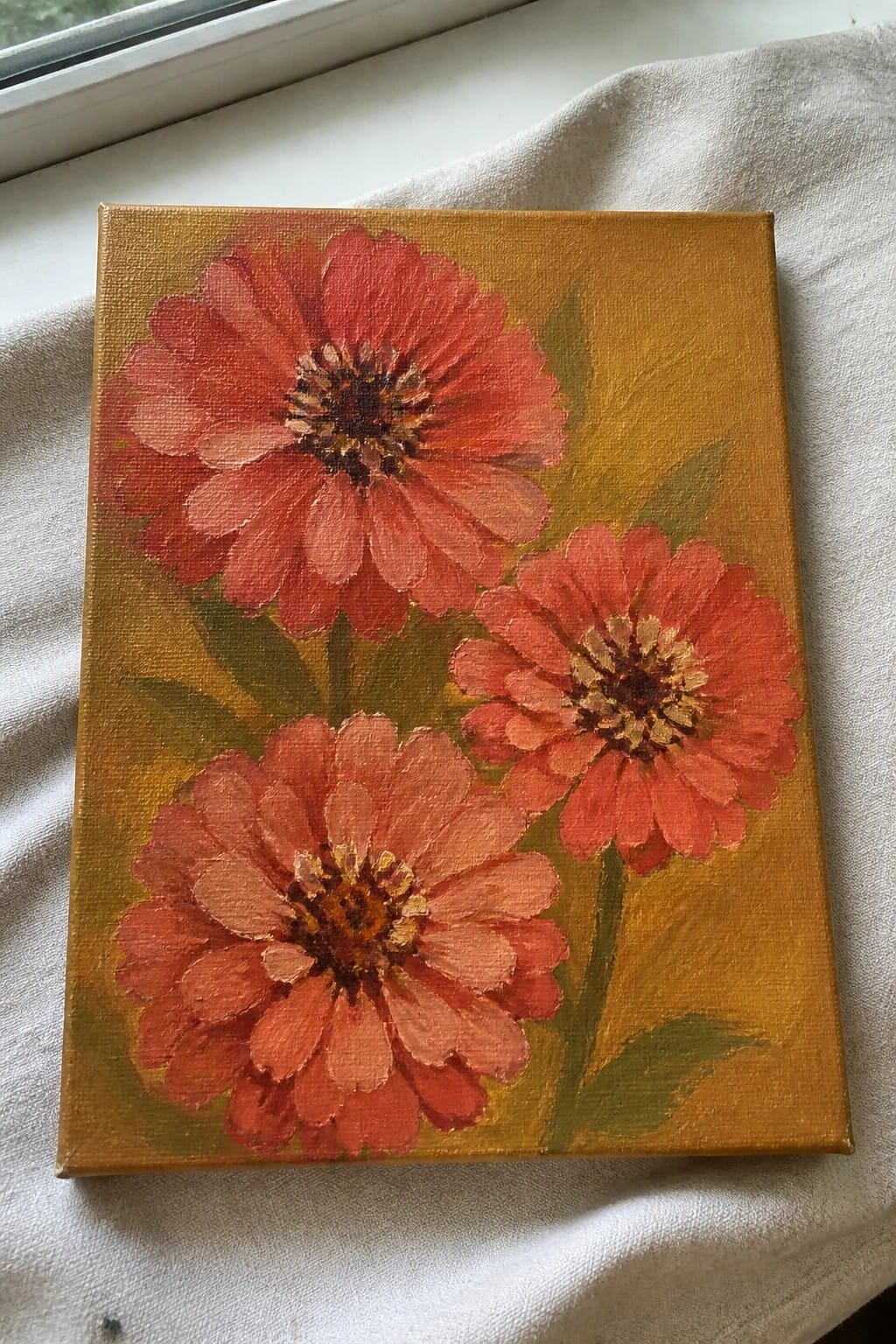 Three red-orange flowers painted on golden-yellow canvas with green leaves