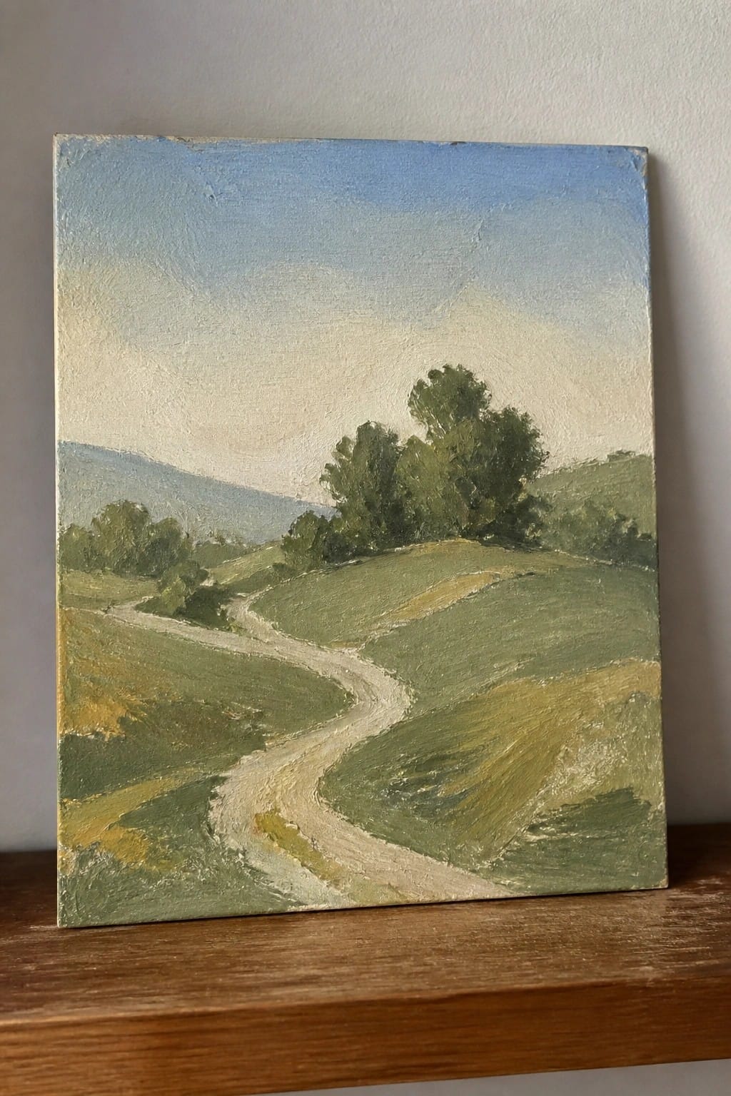 Winding dirt path through rolling green hills with trees under blue sky.