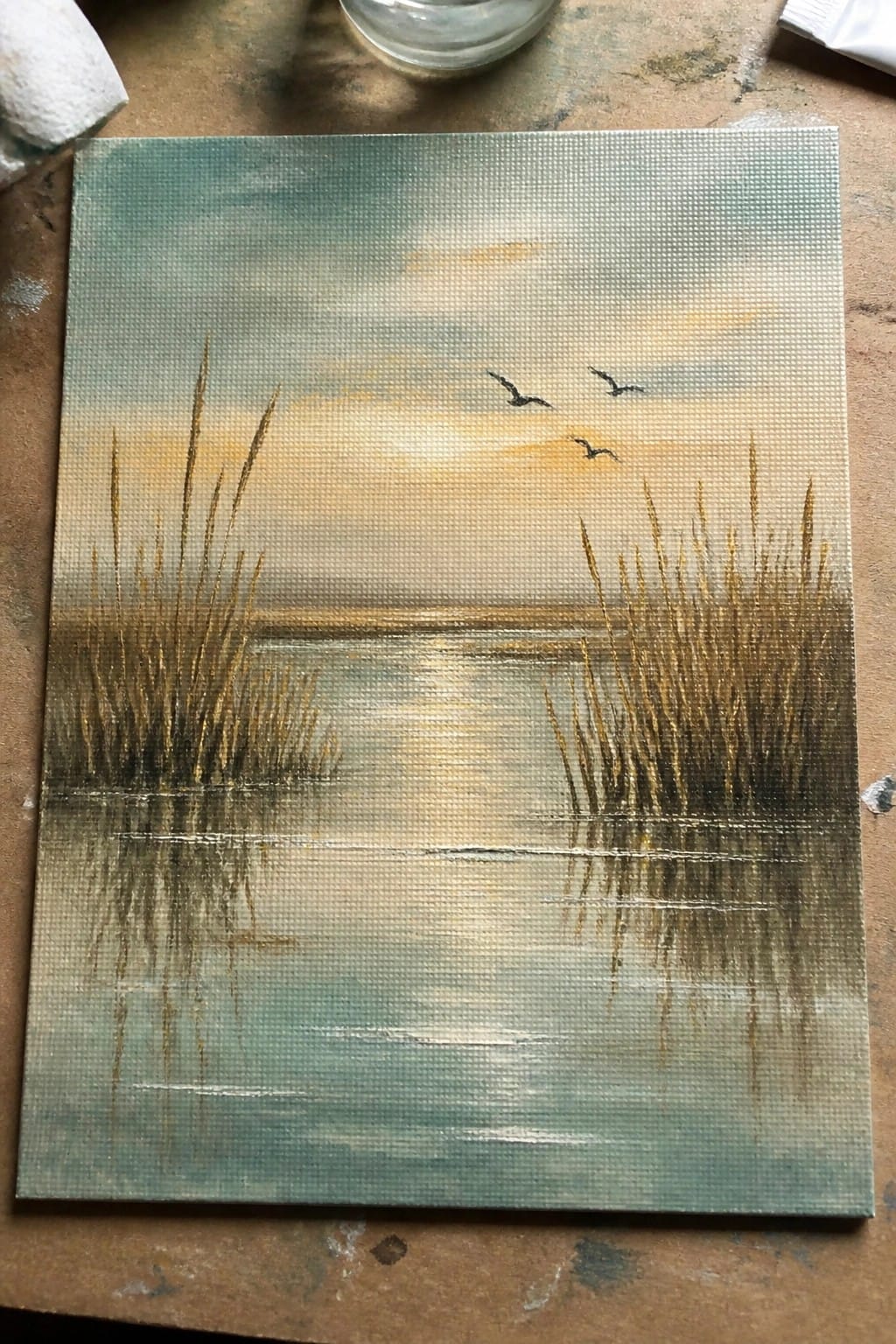 Landscape painting of sunset over water with reeds, reflections, and flying birds.