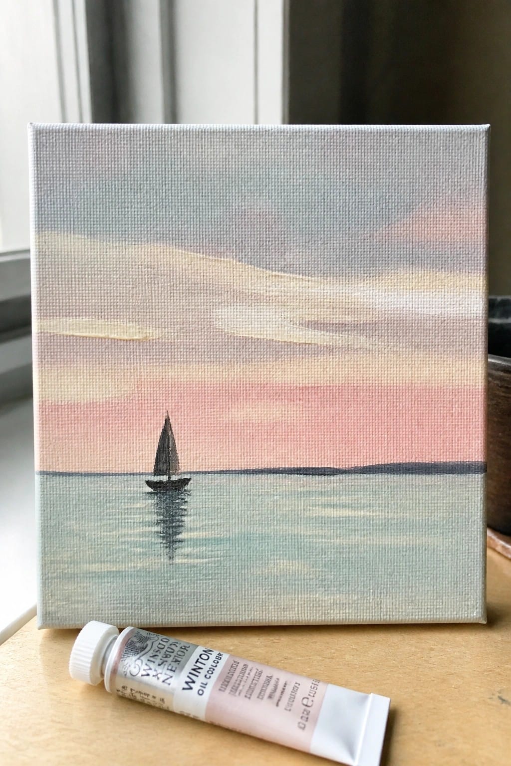 Canvas sailboat painting at sunset beside Winsor & Newton flesh tint oil tube