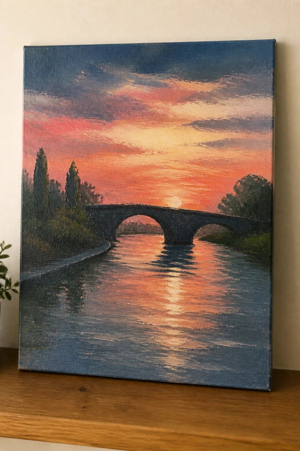 Oil painting of arched bridge over river reflecting vibrant pink-orange sunset sky with trees.