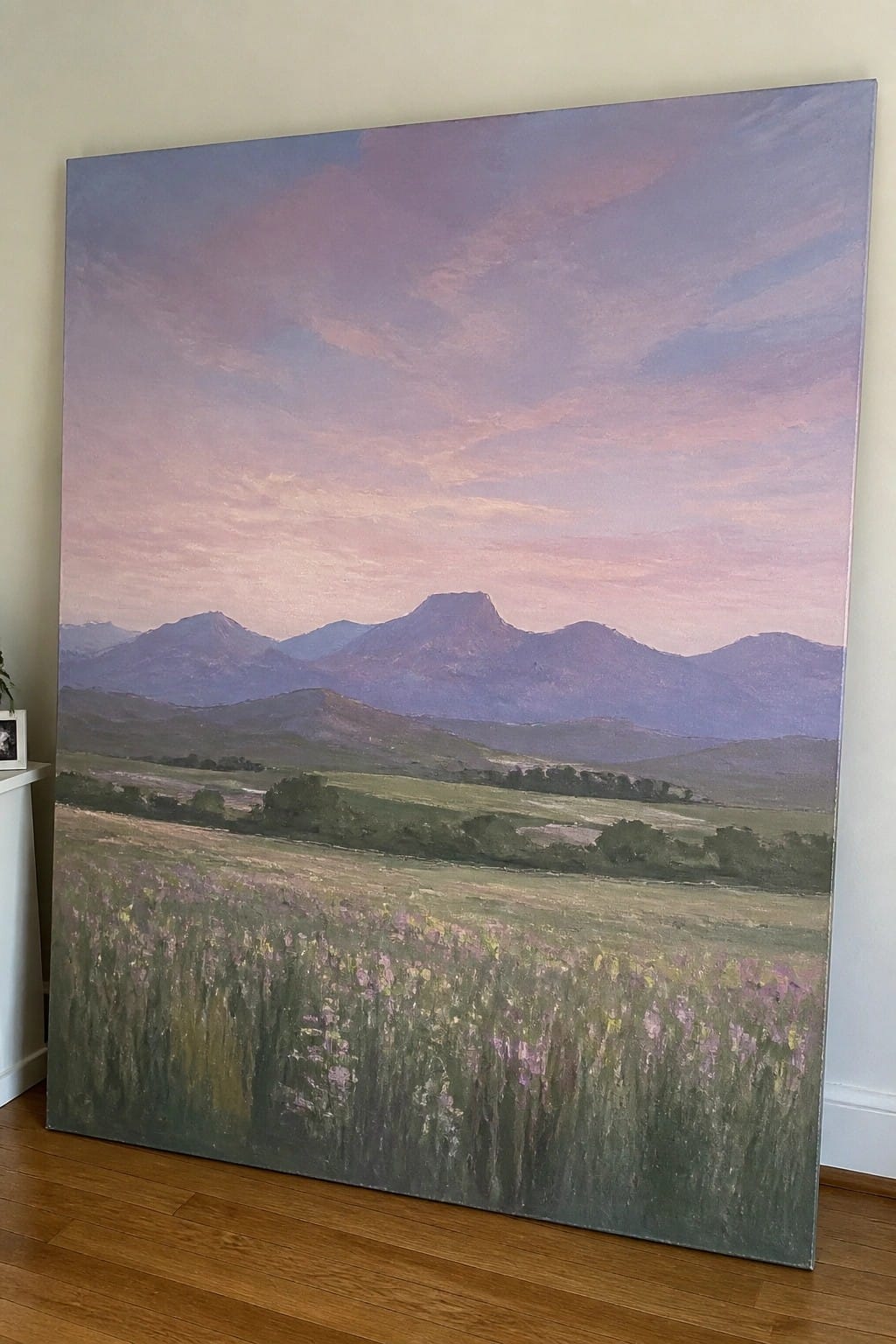 Large landscape painting of mountains under pink-purple sky leaning on wall