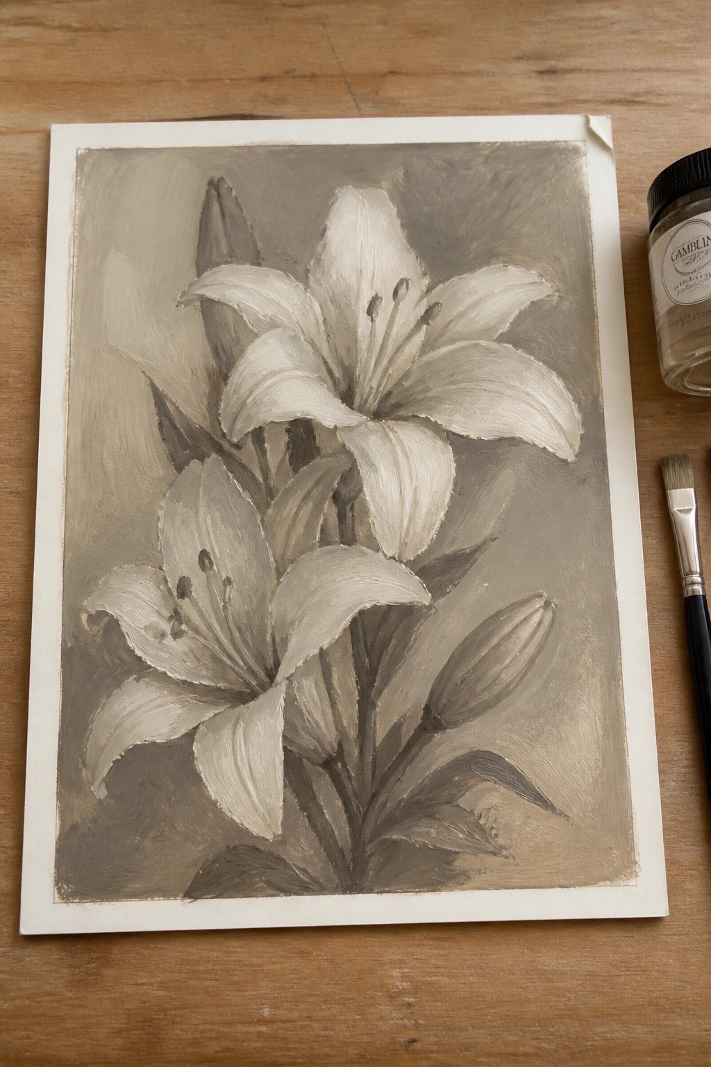 Monochromatic painting of white lilies and buds beside paint jar and brush on wood.