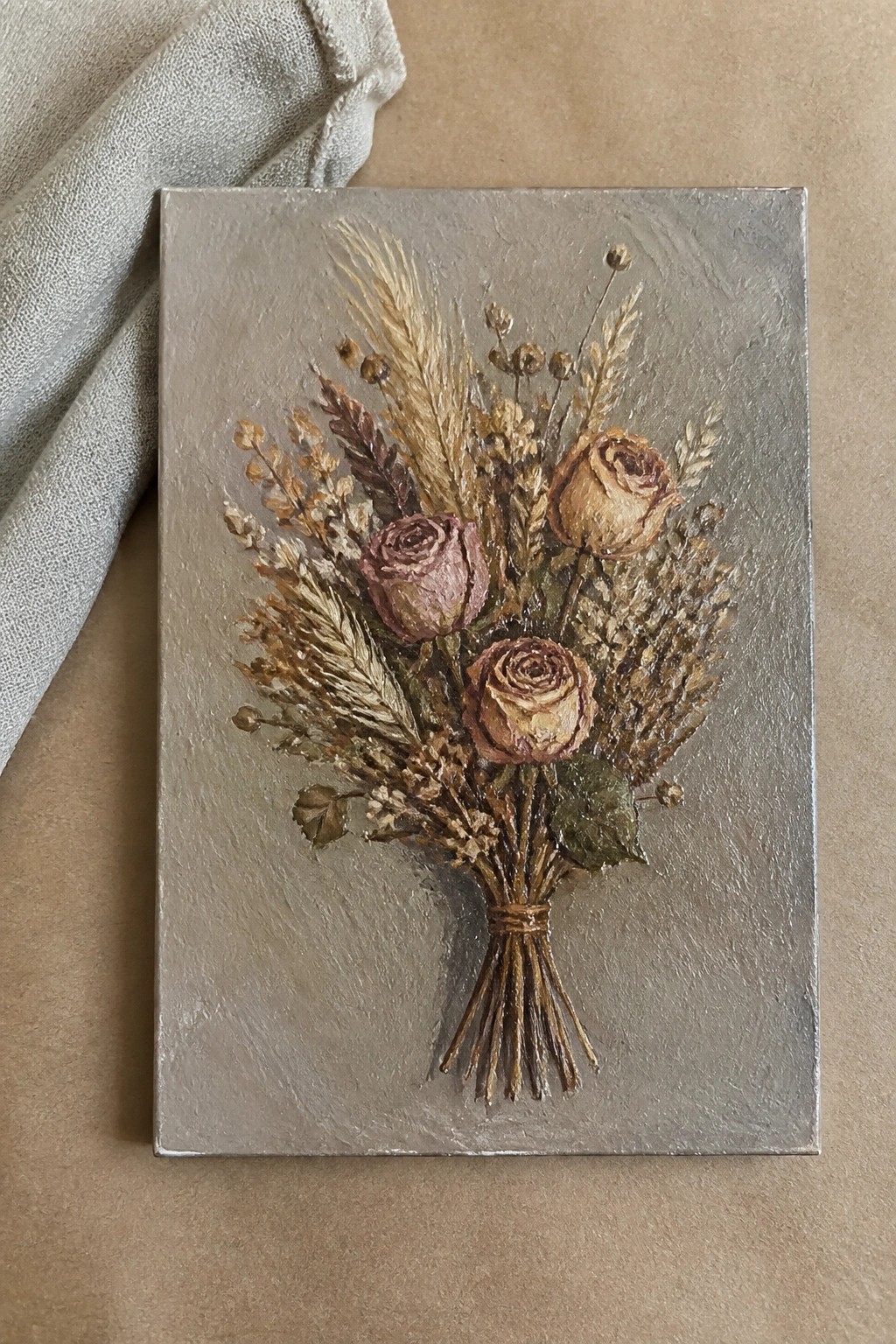 Textured painting of dried roses, wheat, and lavender tied in bouquet on gray canvas beside fabric.