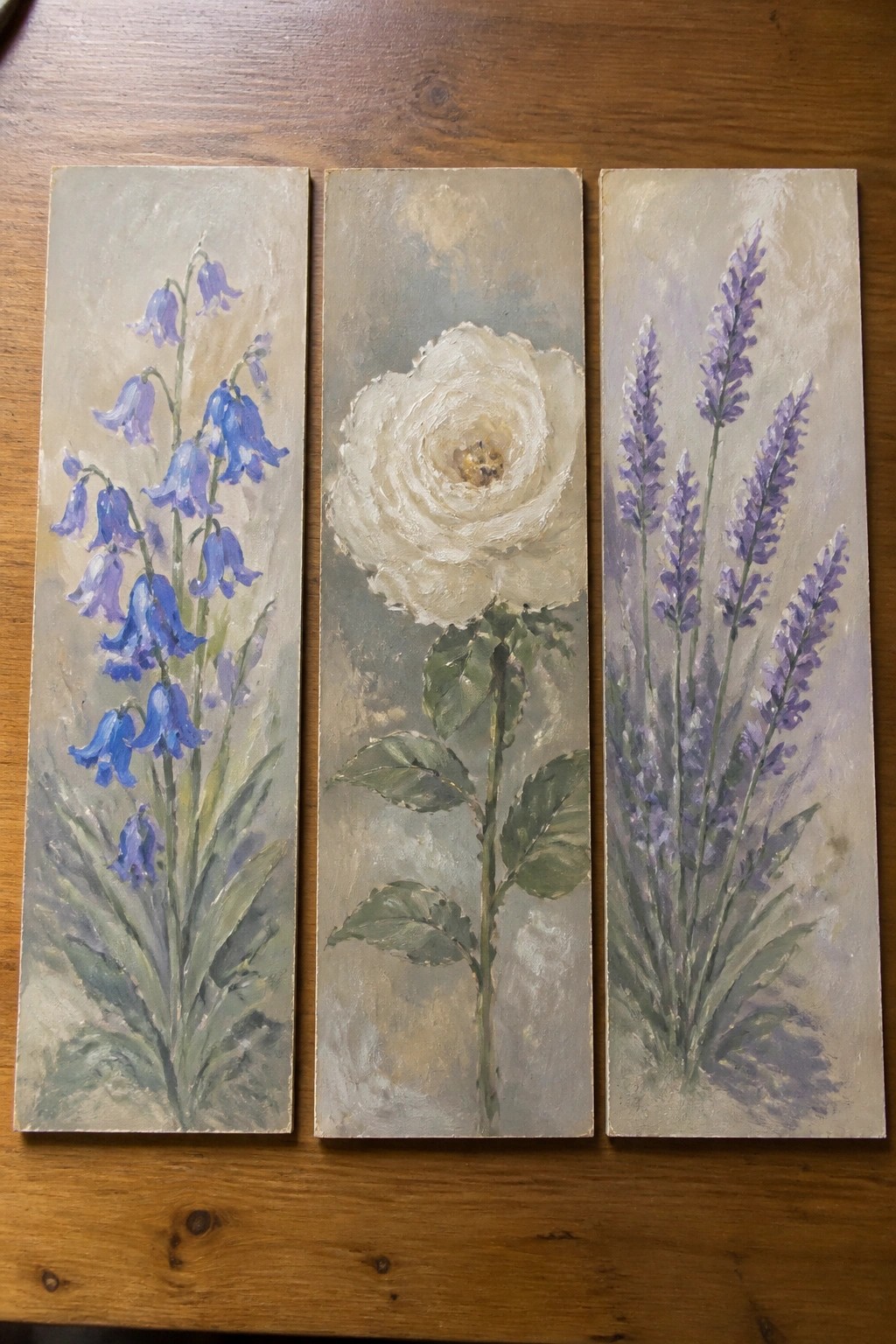 Three painted panels of bluebells, a white rose, and purple lavender on wood.