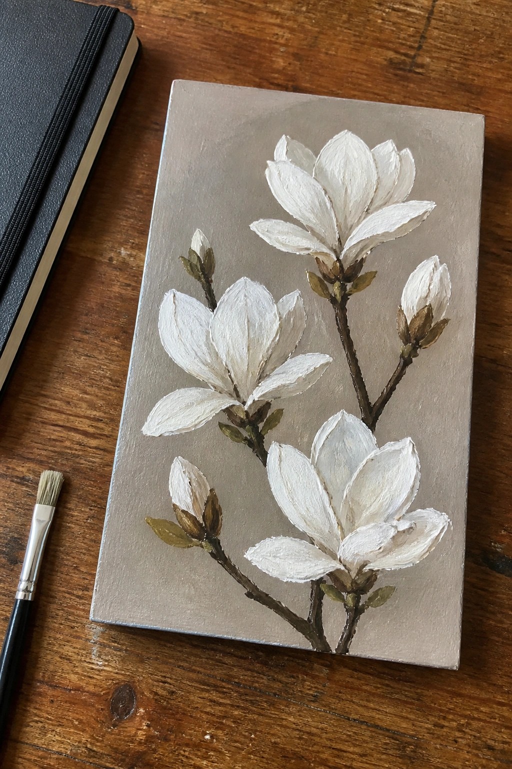 White magnolia painting on canvas with paintbrush and notebook on wooden table