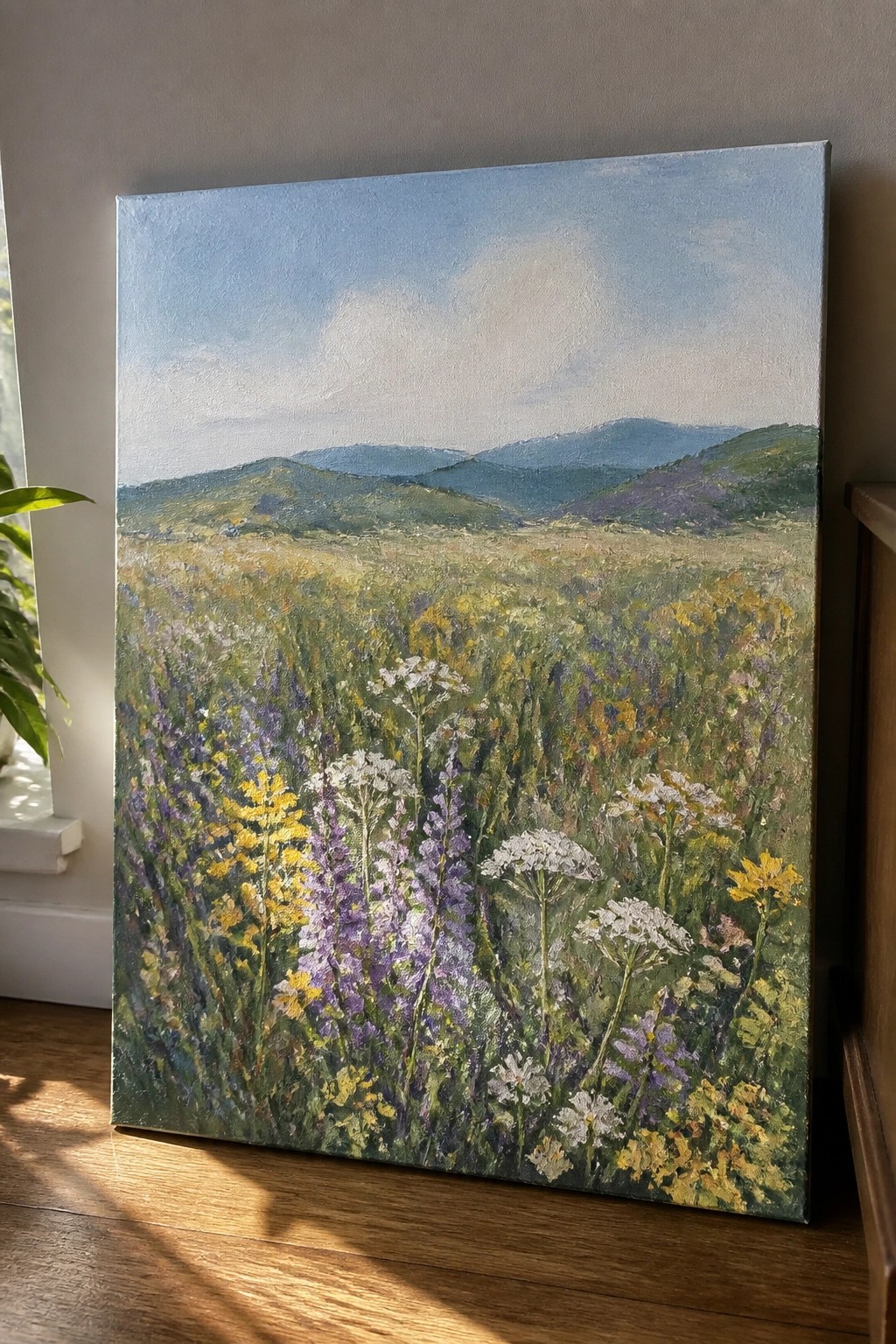 Vibrant wildflower meadow painting with mountains propped on wooden floor against wall
