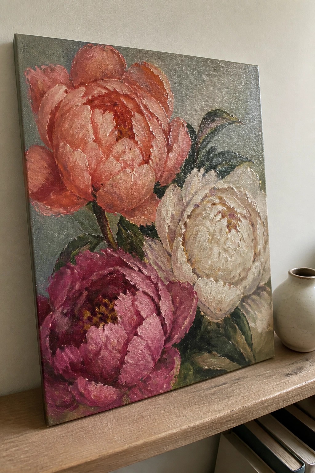 Oil painting of pink, red, white, and magenta peonies on canvas beside a vase.