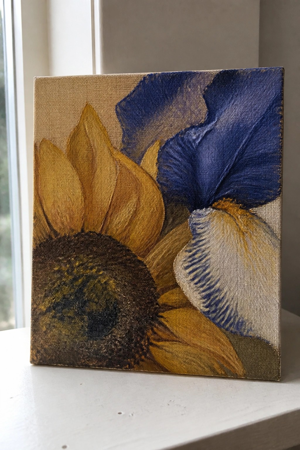 Sunflower and blue iris flowers painted on canvas by a window.
