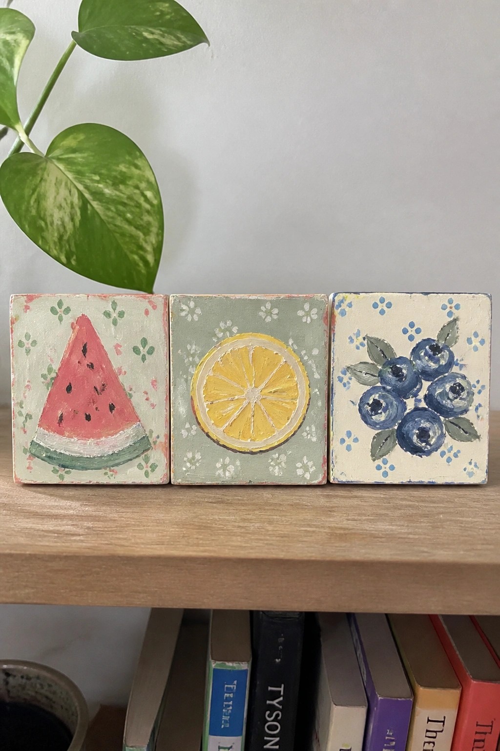 Three hand-painted fruit tiles of watermelon, lemon, and blueberries on wooden shelf