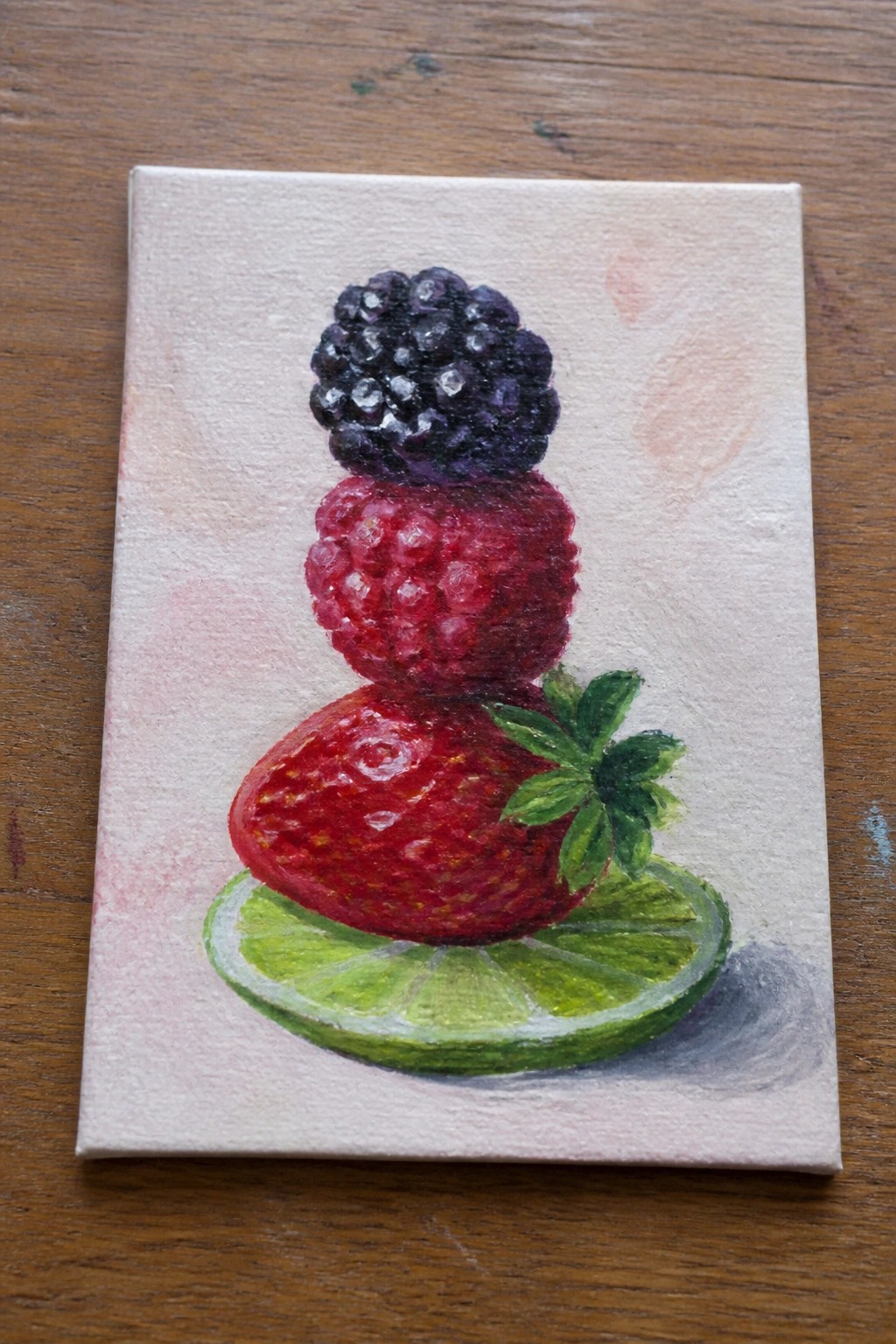 Miniature painting of stacked blackberry, raspberry, and strawberry on lime slice.