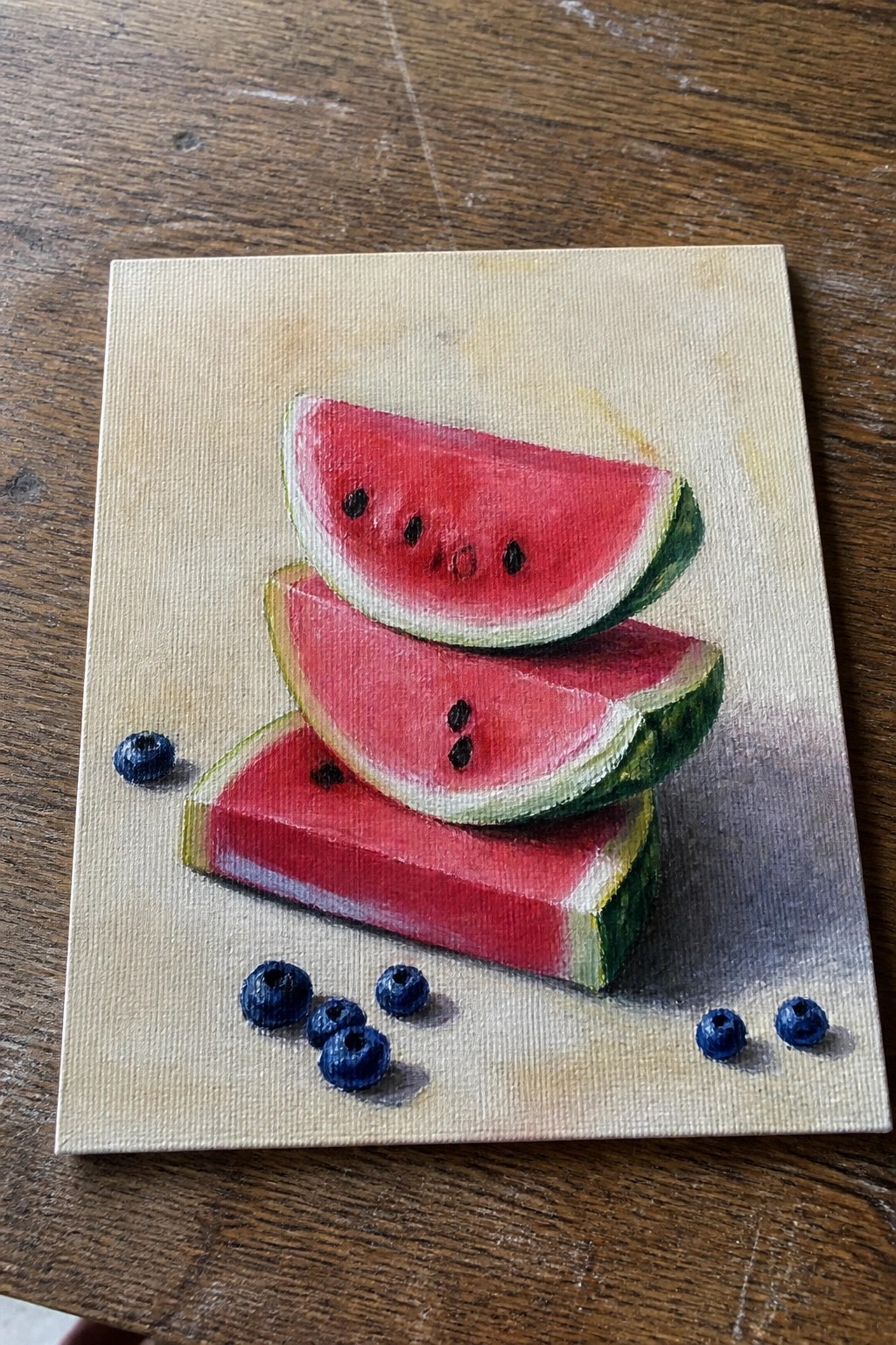Three stacked watermelon slices with scattered blueberries on a canvas still life.