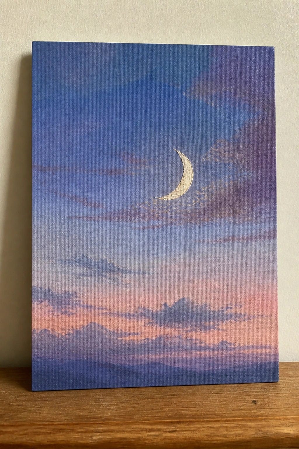 Painting of golden crescent moon in blue-purple sky above pink-orange mountains and clouds
