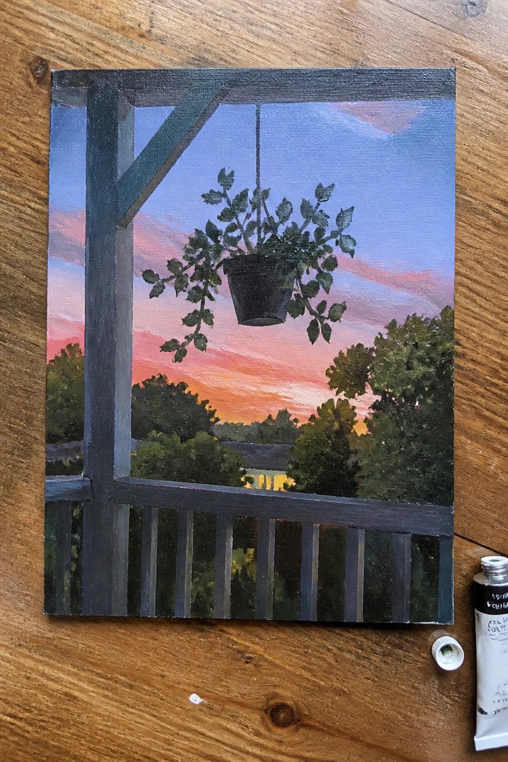 An oil painting of a black hanging plant pot on a dark wooden porch overlooking trees and a pink-orange sunset sky.