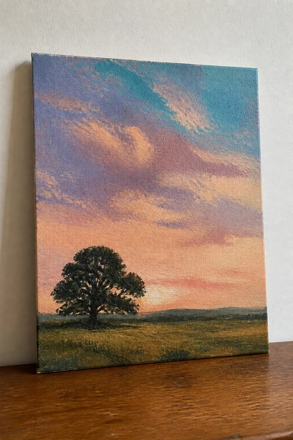 Lone tree in grassy field beneath vibrant pink and blue sunset sky on canvas.