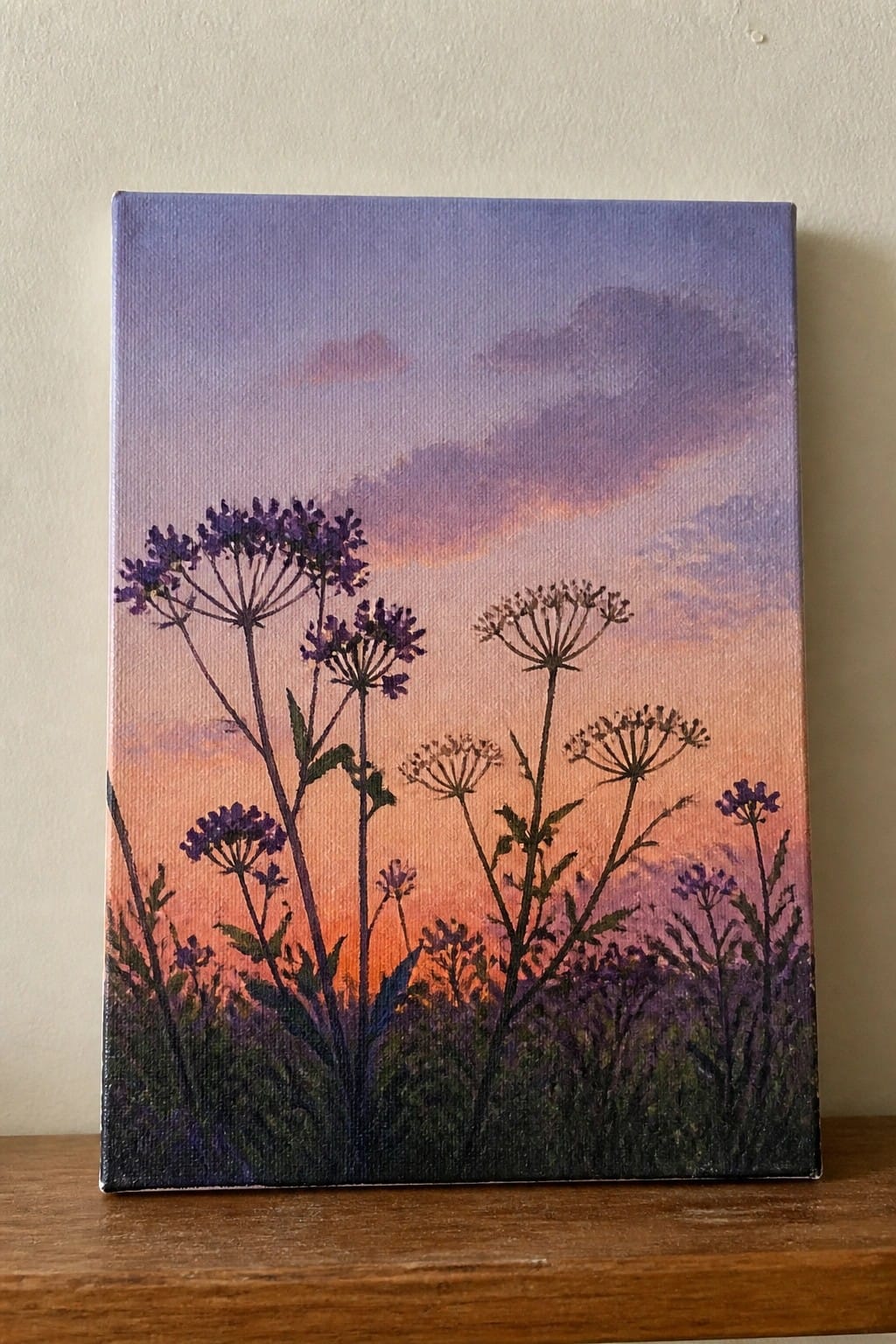 Canvas painting of dark wildflowers silhouetted against vibrant purple-orange sunset sky on wood.