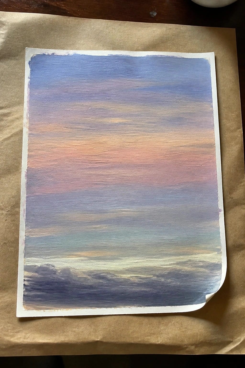Watercolor painting of sunset sky with blue, orange, pink horizontal brushstrokes on paper.