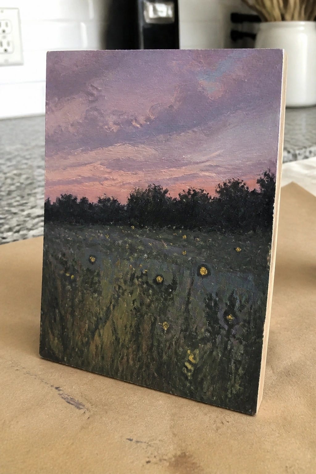 Impressionistic oil painting on wood of purple-pink sunset over dark meadow with yellow flowers