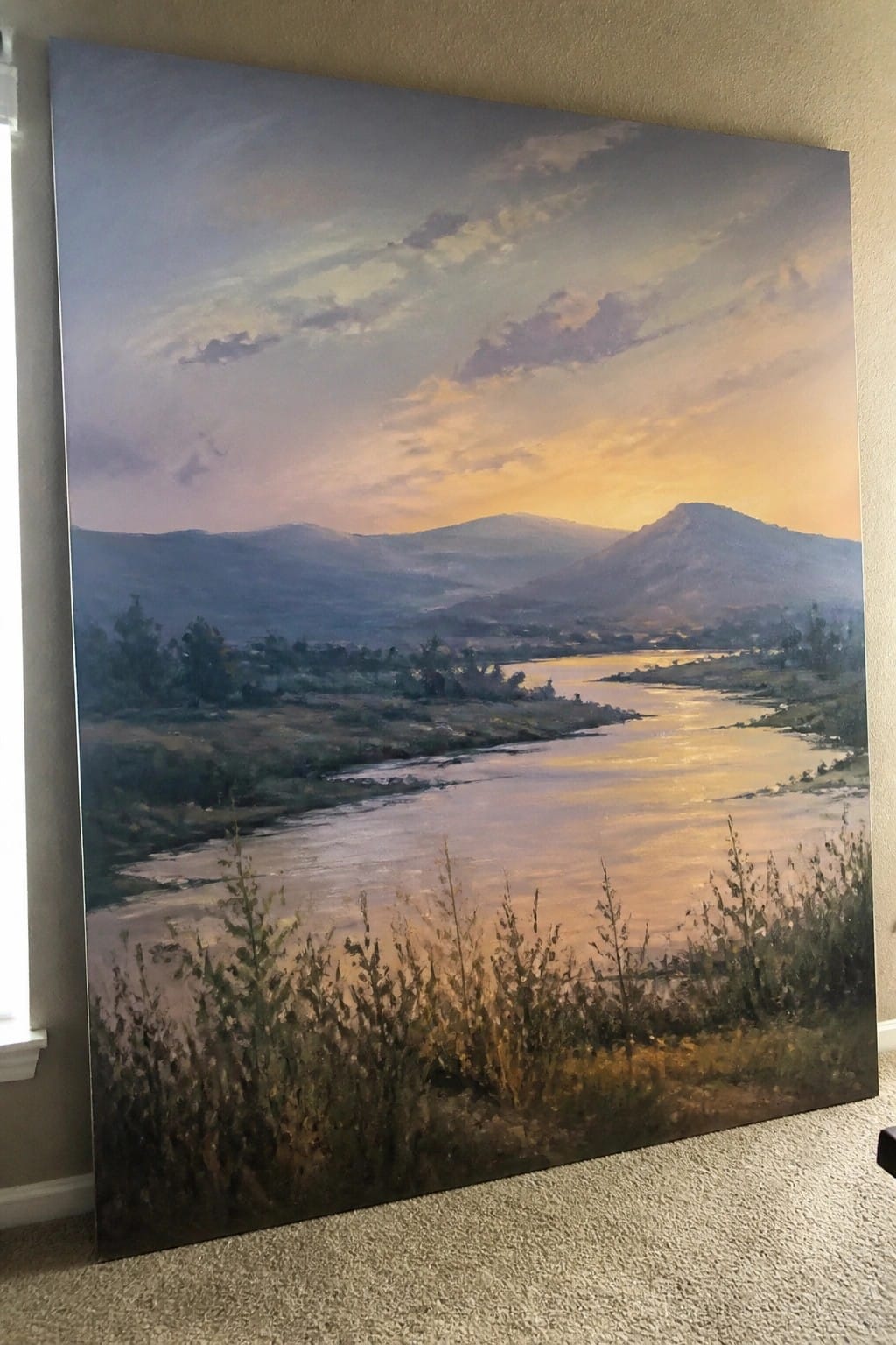 Large landscape painting of winding river reflecting golden sunset, leaning on wall