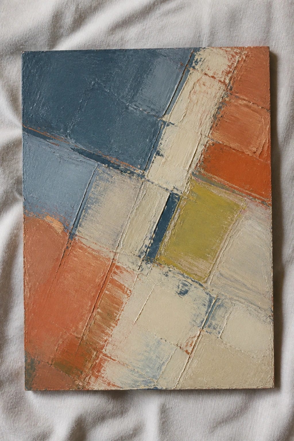 Abstract painting with blue, orange, beige, and yellow geometric shapes on white fabric
