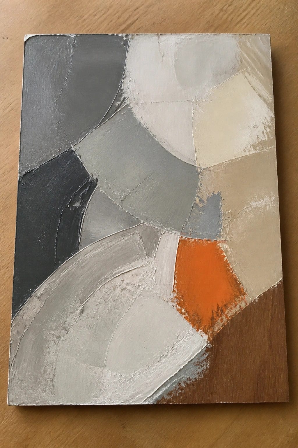 Abstract painting with textured gray, white, beige shapes and orange accent on wood.