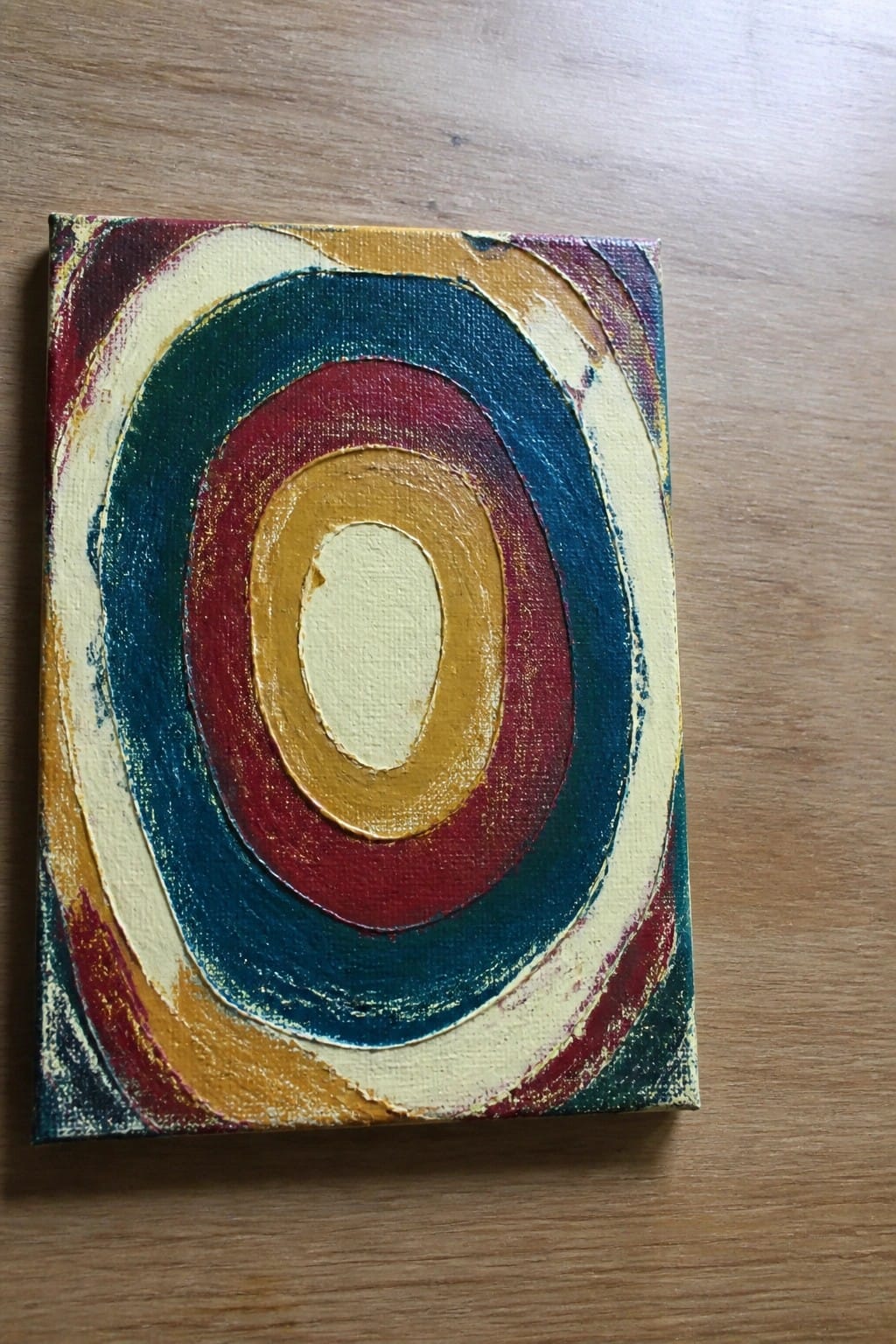 Abstract canvas with vibrant concentric ovals in red, blue, and yellow on wood.