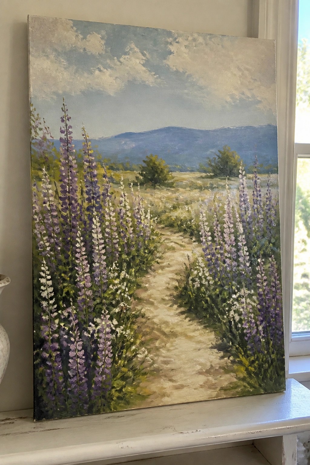 Oil painting of purple wildflowers along a dirt path toward misty blue mountains