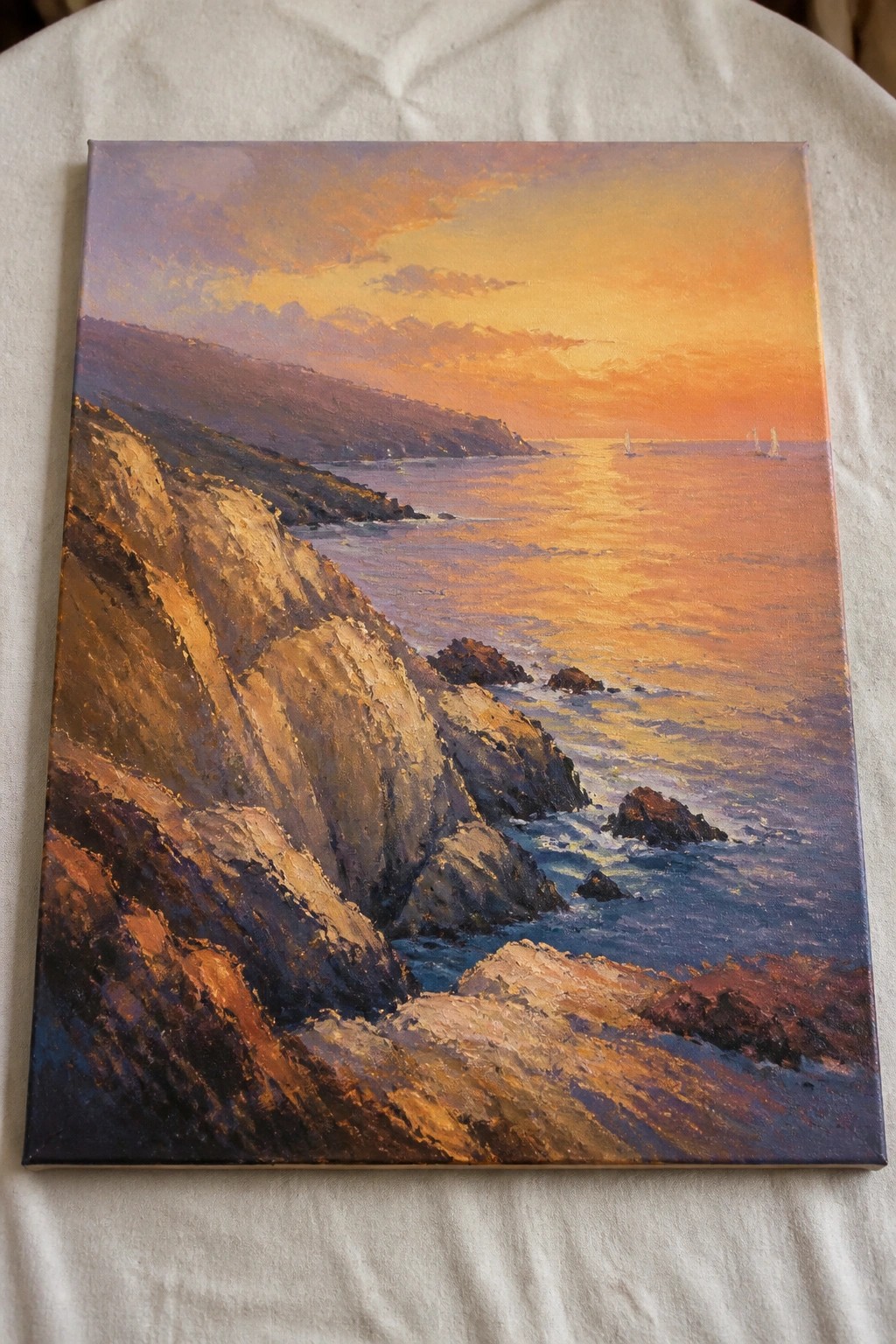 Colorful sunset over rugged cliffs and rocky ocean shore with sailboats on horizon