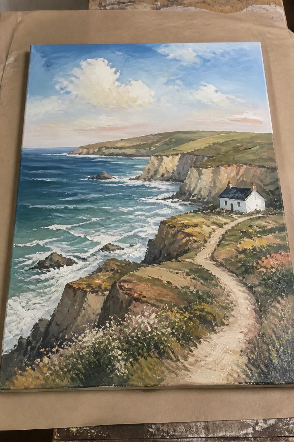 Painting of white cottage on cliffs by wavy blue sea with winding path